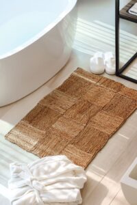 Bright bathroom setting featuring woven mat, bathtub, towel, and slippers.