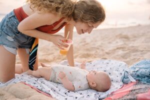 A joyful mother enjoys a sunny day at the beach interacting with her baby, creating warm family memories.