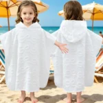 Model photo of white cotton children hooded poncho towel, little girl showing front and back wearing effect on the beach.