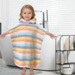 Girl aged 2-4 wearing the pastel rainbow striped hooded towel poncho in a bright bathroom with a towel ladder