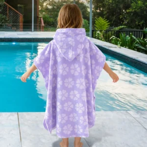 Child wearing an aqua purple striped hooded poncho towel beside a swimming pool