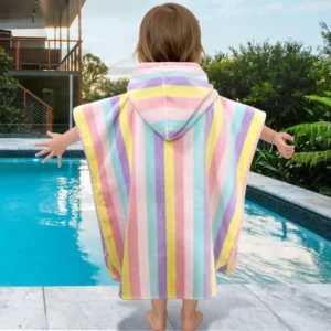 Toddler wearing a rainbow stripe hooded towel beside a swimming pool