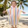 Toddler wearing a colorful rainbow stripe hooded towel at the beach